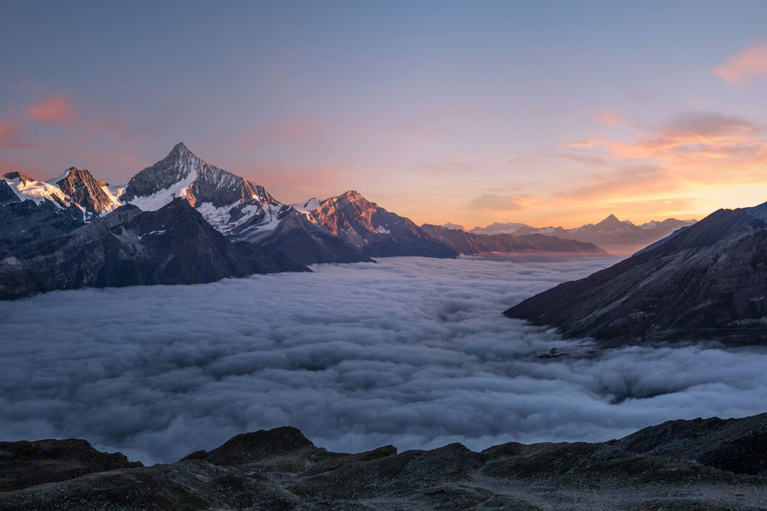 Sunrise over mountain peaks, clouds covering a valley below