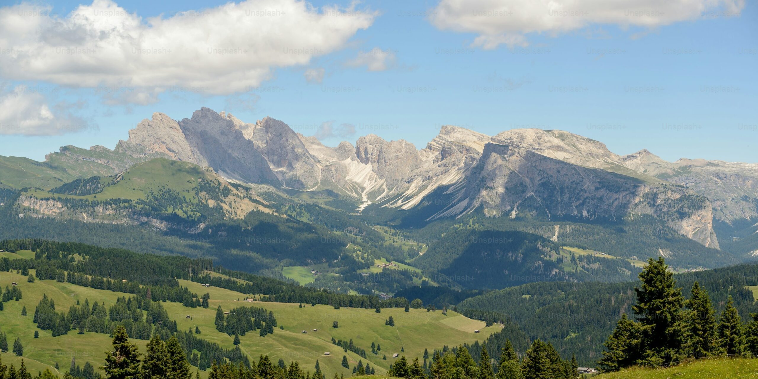 A scenic valley with lush greenery and majestic mountains in the background under a partly cloudy sky.