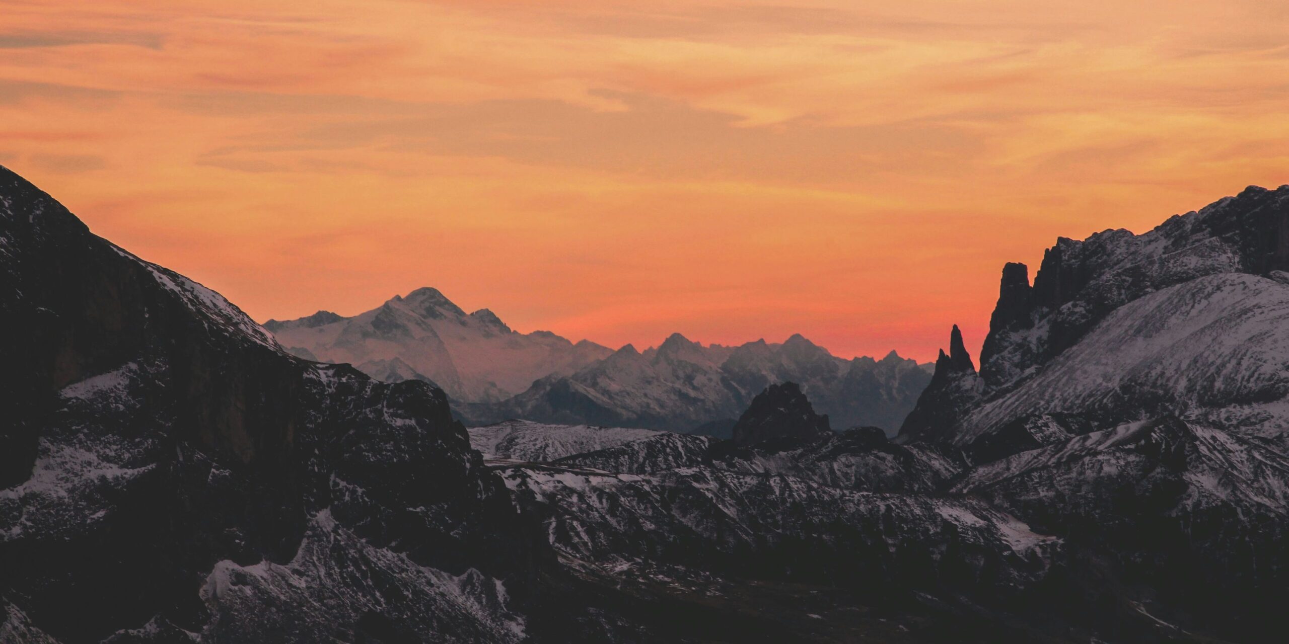 Snowy mountain landscape at sunset with orange sky.