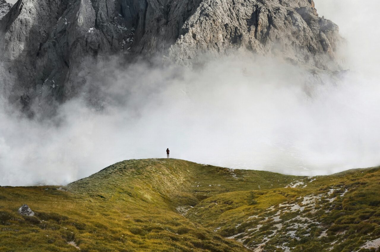 Solitary figure stands on a misty mountain hill, surrounded by fog