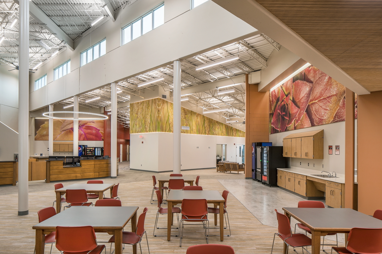 Modern office space with high ceilings, colorful murals, red chairs, wooden tables, and a kitchen area with vending machines
