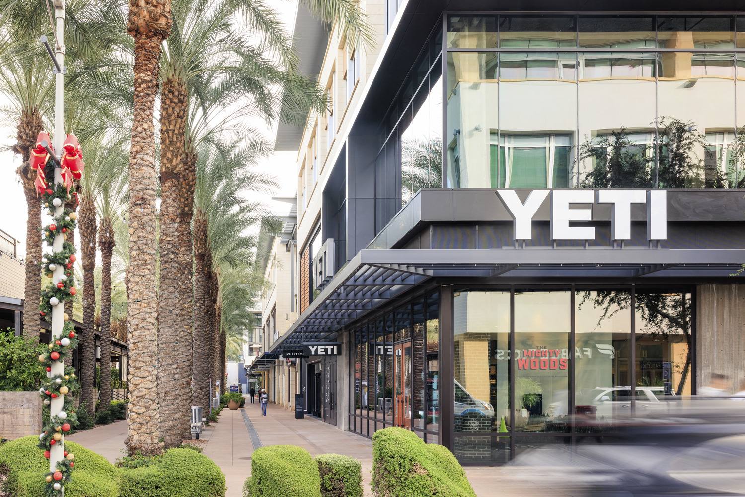YETI storefront with reflective glass under palm trees, holiday decorations on lamppost, and people walking
